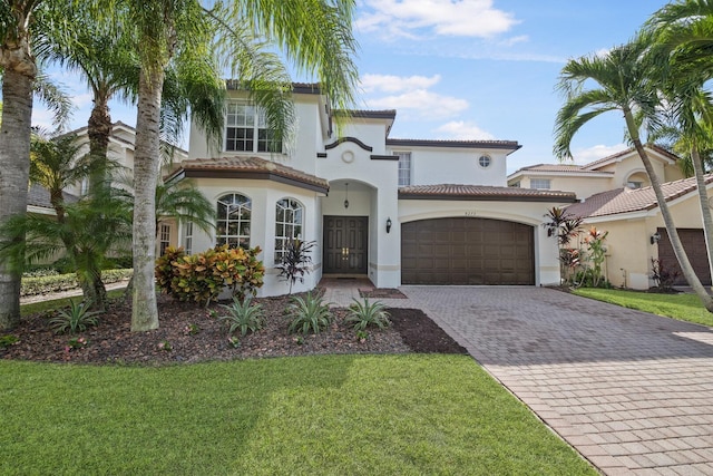 mediterranean / spanish-style house with a front lawn, a tile roof, stucco siding, decorative driveway, and an attached garage