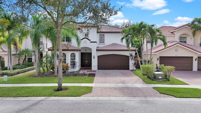 mediterranean / spanish house with a tile roof, decorative driveway, a front lawn, and stucco siding