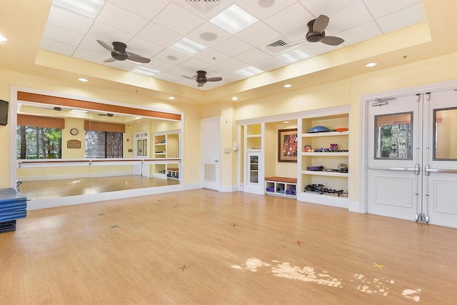 exercise area with a tray ceiling, ceiling fan, and wood finished floors