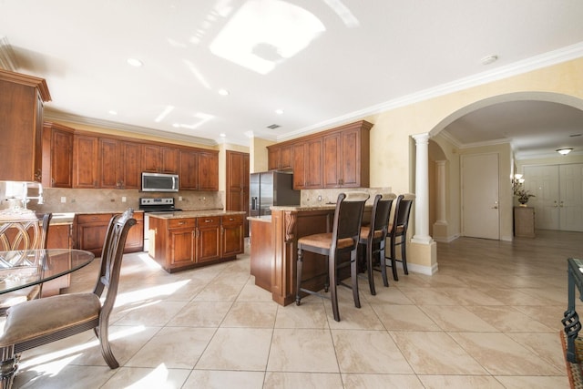 kitchen with tasteful backsplash, arched walkways, appliances with stainless steel finishes, a peninsula, and decorative columns