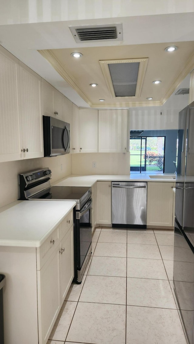 kitchen with crown molding, light tile patterned floors, a tray ceiling, stainless steel appliances, and cream cabinetry