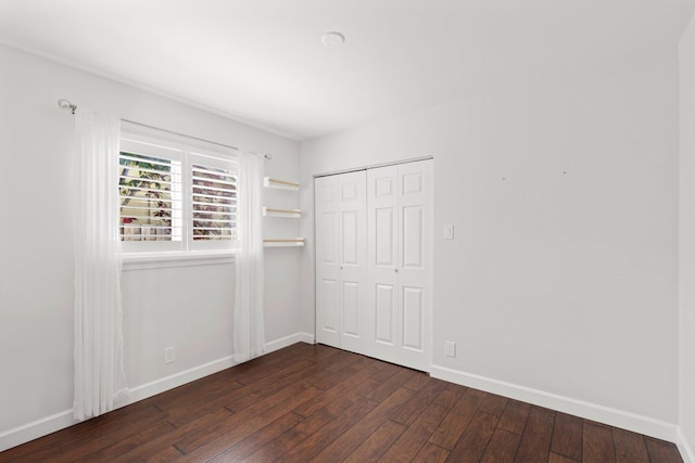 unfurnished bedroom with a closet, dark wood finished floors, and baseboards