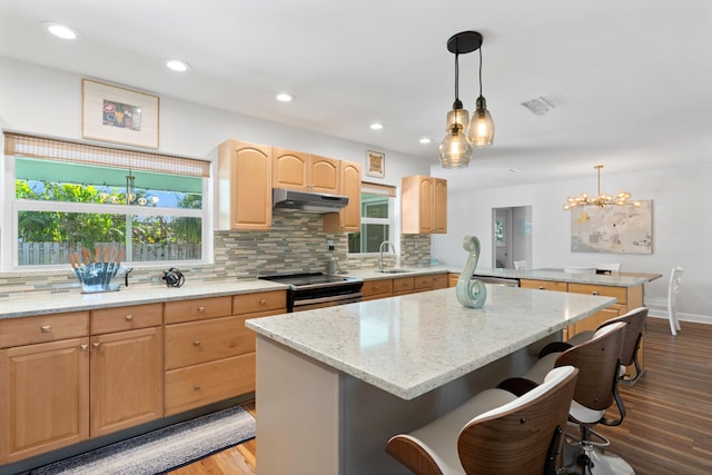 kitchen with appliances with stainless steel finishes, a breakfast bar area, a center island, light stone countertops, and under cabinet range hood