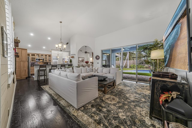 living room with dark wood-style floors, recessed lighting, arched walkways, and ceiling fan with notable chandelier