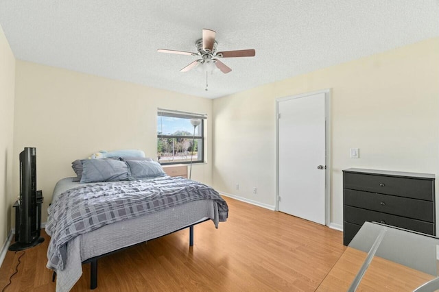 bedroom with light wood-type flooring, ceiling fan, a textured ceiling, and baseboards