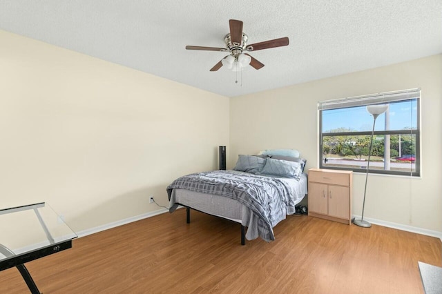 bedroom featuring light wood-style floors, ceiling fan, a textured ceiling, and baseboards