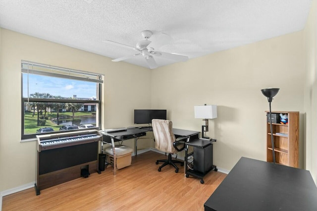 home office with a textured ceiling, light wood-type flooring, a ceiling fan, and baseboards