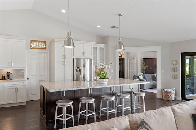 kitchen featuring a breakfast bar, white cabinetry, stainless steel refrigerator with ice dispenser, a center island with sink, and decorative light fixtures