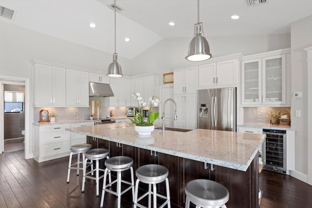 kitchen with white cabinetry, sink, stainless steel fridge, beverage cooler, and a large island with sink