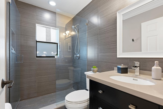 bathroom with vanity, tiled shower, tile walls, and toilet