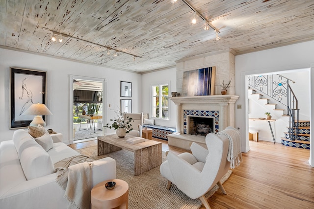 living room featuring a tiled fireplace, wooden ceiling, light wood-style flooring, stairway, and track lighting