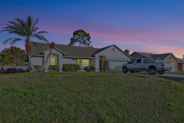 single story home featuring a lawn, an attached garage, and stucco siding