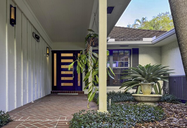 property entrance with central AC and roof with shingles