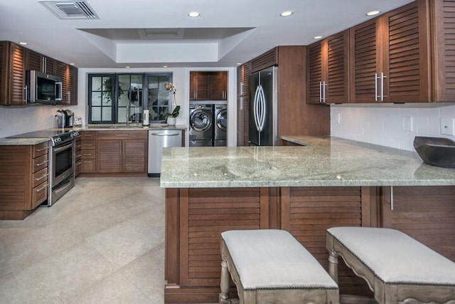 kitchen with a peninsula, separate washer and dryer, stainless steel appliances, visible vents, and a raised ceiling