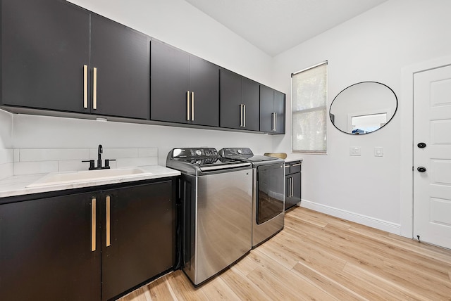 laundry room with light hardwood / wood-style floors, sink, washing machine and dryer, and cabinets