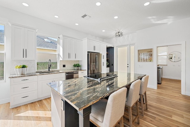 kitchen with dishwashing machine, stainless steel fridge, dark stone countertops, white cabinetry, and a kitchen island