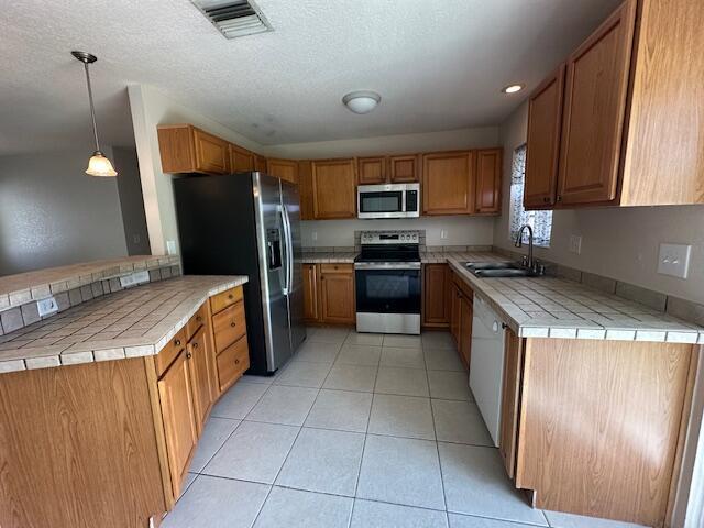 kitchen with sink, tile countertops, hanging light fixtures, appliances with stainless steel finishes, and kitchen peninsula