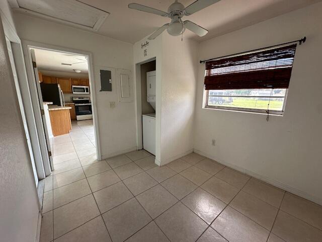 tiled empty room featuring electric panel, ceiling fan, and stacked washer / dryer