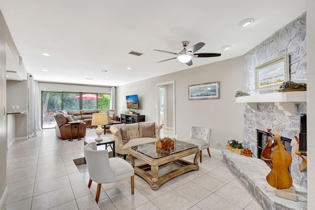 tiled living room with ceiling fan and a stone fireplace