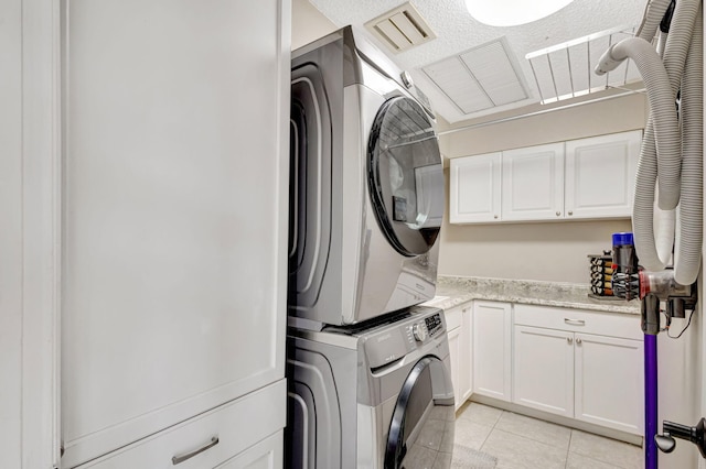 laundry room featuring cabinets, light tile patterned flooring, stacked washer and clothes dryer, and a textured ceiling