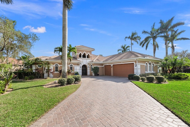 mediterranean / spanish house with a front lawn, a tiled roof, stucco siding, decorative driveway, and a garage