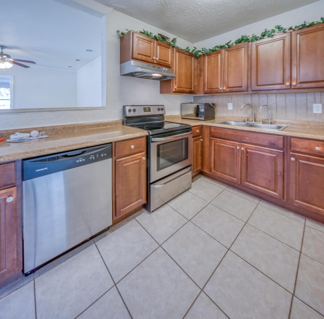 kitchen with a textured ceiling, under cabinet range hood, stainless steel appliances, a sink, and light countertops