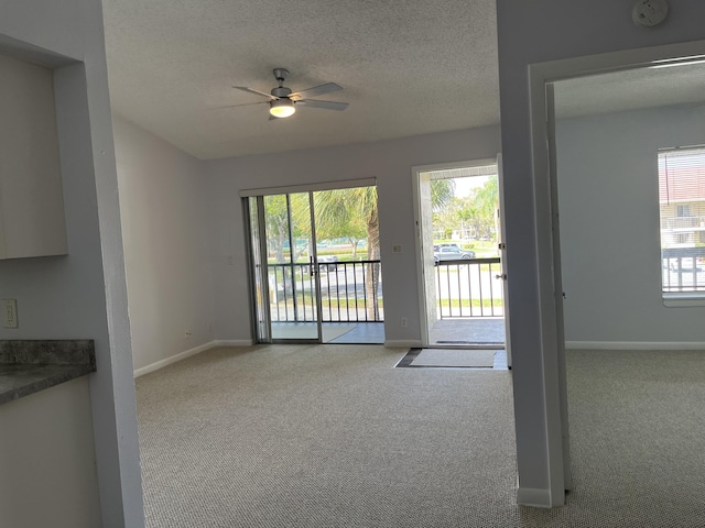 interior space with a ceiling fan, baseboards, a textured ceiling, and light colored carpet