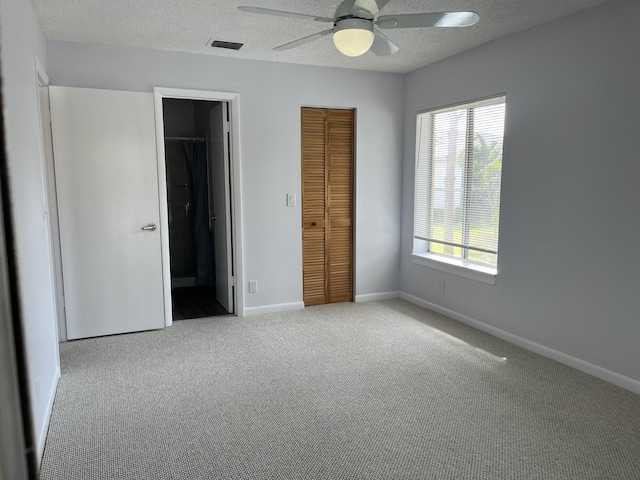 unfurnished bedroom with a closet, visible vents, light carpet, a textured ceiling, and baseboards