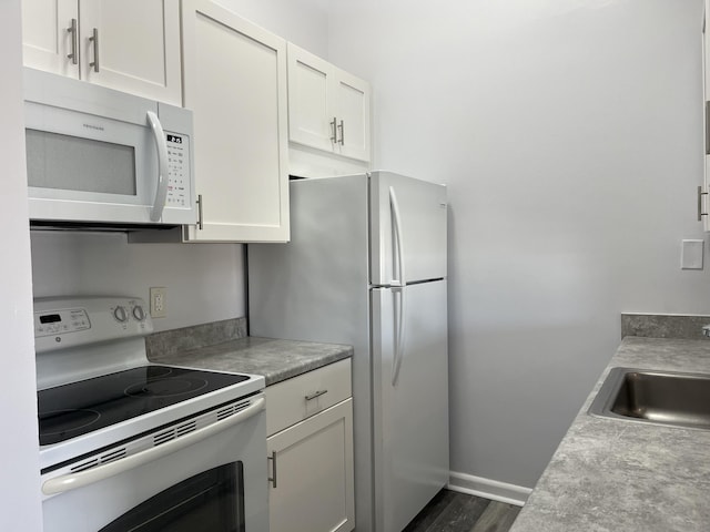 kitchen featuring white appliances, white cabinets, dark wood finished floors, light countertops, and a sink