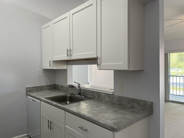 kitchen with dishwasher, dark countertops, a sink, and white cabinets