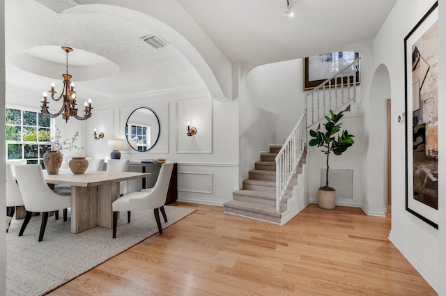 dining area with a raised ceiling, an inviting chandelier, and light hardwood / wood-style flooring