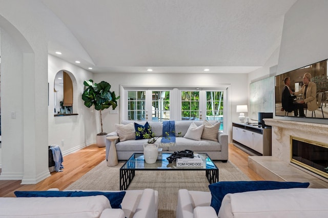 living room with lofted ceiling, a premium fireplace, light hardwood / wood-style flooring, and french doors