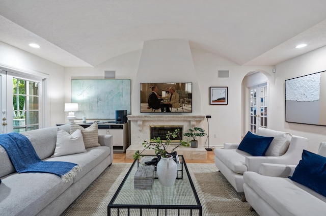 living room featuring vaulted ceiling, hardwood / wood-style floors, a high end fireplace, and french doors