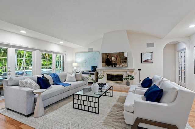 living room with lofted ceiling, a fireplace, light hardwood / wood-style flooring, and french doors