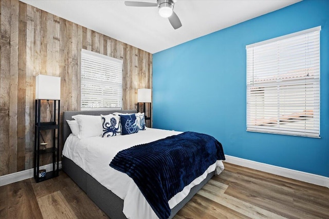 bedroom with dark hardwood / wood-style floors, ceiling fan, and wood walls