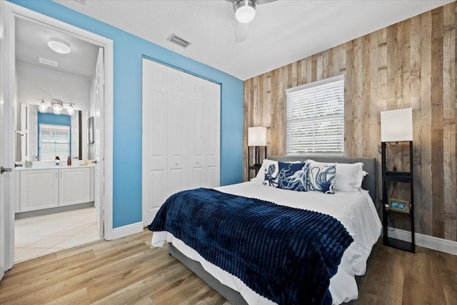 bedroom featuring ceiling fan, hardwood / wood-style floors, wooden walls, connected bathroom, and a closet