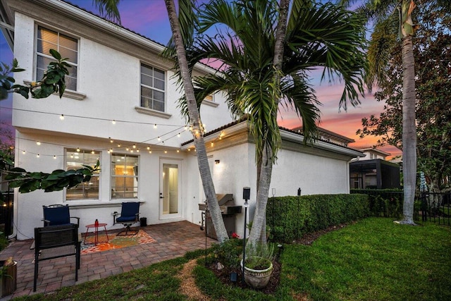 back house at dusk with a patio and a lawn