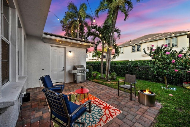 patio terrace at dusk featuring area for grilling and a fire pit