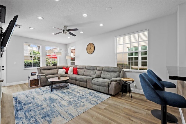 living room with ceiling fan, a textured ceiling, and light wood-type flooring