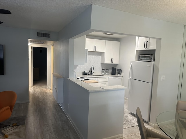 kitchen with sink, white appliances, hardwood / wood-style flooring, white cabinetry, and decorative backsplash