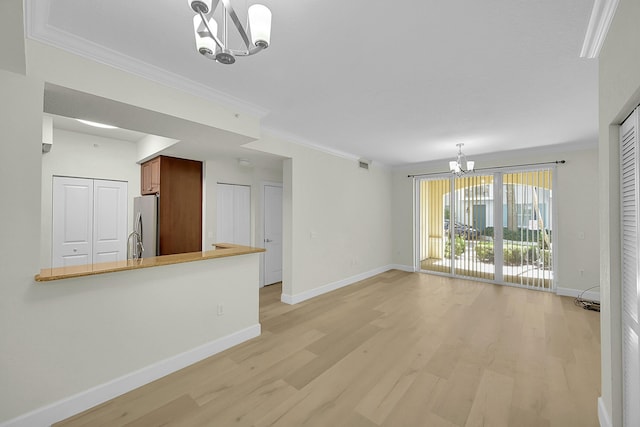 unfurnished living room featuring baseboards, light wood-style floors, a chandelier, and ornamental molding