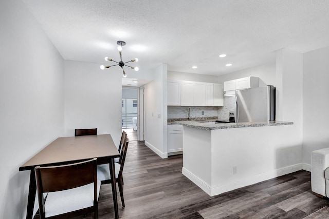 kitchen with white cabinetry, stainless steel fridge, dark hardwood / wood-style flooring, light stone counters, and kitchen peninsula