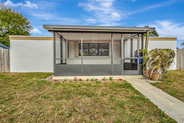 rear view of property featuring a sunroom, fence, and a lawn