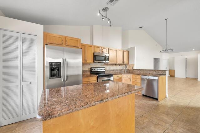 kitchen with appliances with stainless steel finishes, stone countertops, pendant lighting, tasteful backsplash, and kitchen peninsula