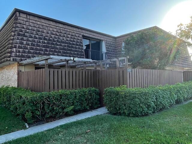 view of side of home featuring brick siding, fence, and mansard roof