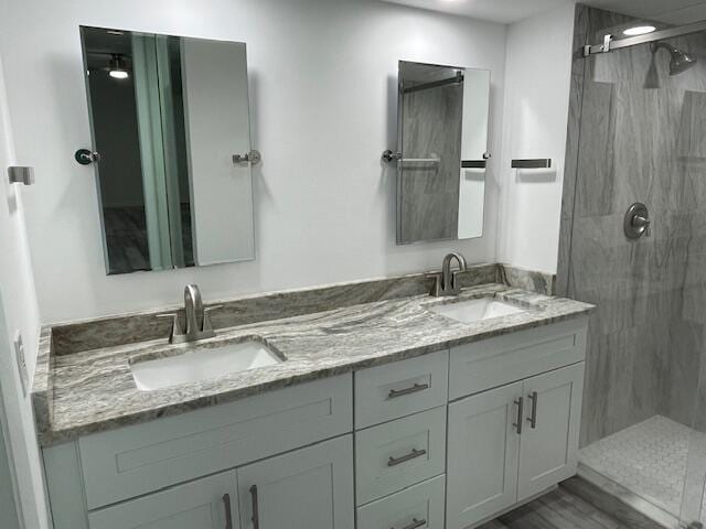 bathroom featuring wood finished floors, a sink, a marble finish shower, and double vanity