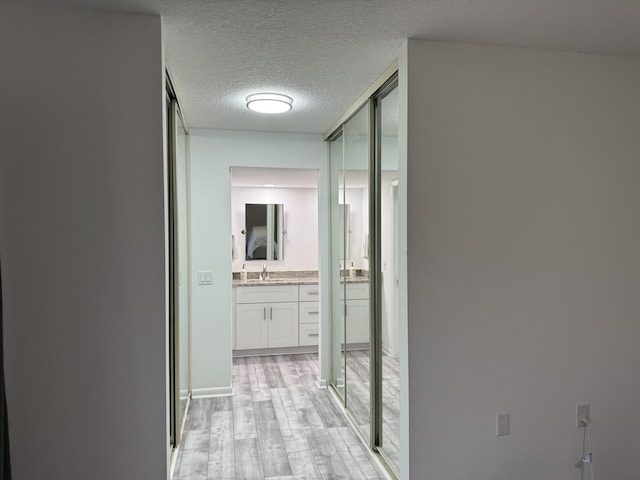 hallway featuring light wood-type flooring, a sink, and a textured ceiling