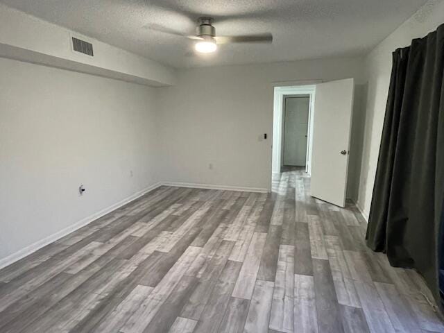 spare room featuring wood finished floors, a textured ceiling, a ceiling fan, and visible vents