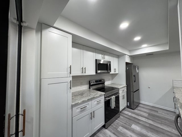 kitchen with light stone counters, stainless steel appliances, white cabinets, backsplash, and light wood finished floors