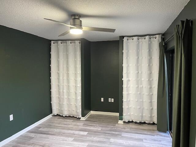 unfurnished room with ceiling fan, baseboards, wood finished floors, and a textured ceiling